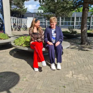 Twee FijnThuis-hulpen praten en lachen samen op een bankje buiten bij ViVa! Zorggroe