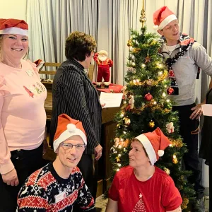 ViVa!-collega’s zingen samen kerstliedjes rond een versierde kerstboom. Ze dragen kerstmutsen, lachen en houden songteksten vast. De sfeer is gezellig, warm en vol aandacht tijdens de feestdagen bij ViVa! Zorggroep.