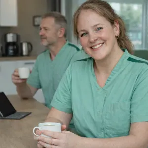 Verpleegkundige woonzorg met koffie en collega op achtergrond