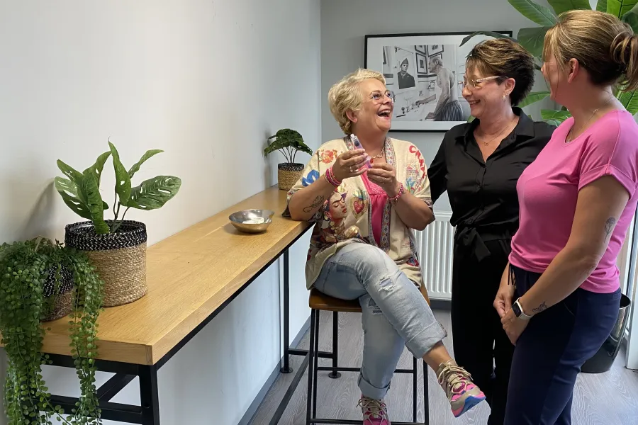 Drie collega’s lachen samen tijdens een gesprek in een gezellige kantoorruimte bij ViVa! Zorggroep