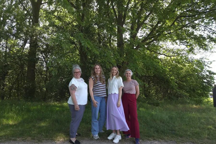 Team recruitment poseert voor een bosrijke achtergrond, vier collega's staan lachend op een mooie zomerdag voor de camera